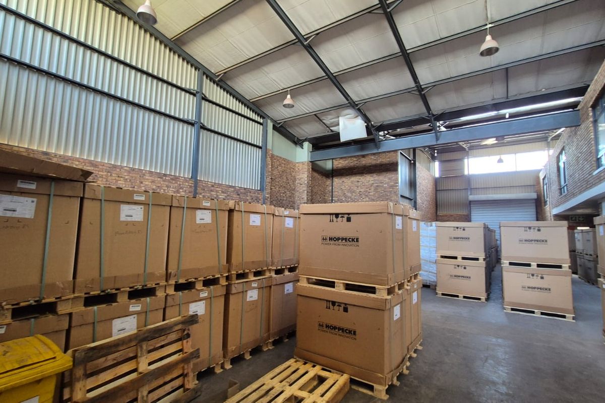 Spacious industrial warehouse unit featuring high ceilings with exposed steel trusses, face brick walls, concrete flooring, and a large roller shutter door.