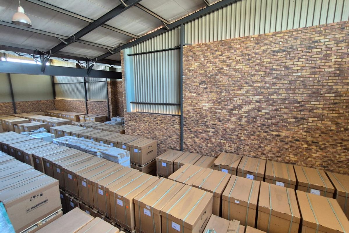 Spacious industrial warehouse area featuring exposed steel roof trusses, corrugated metal cladding, and a decorative face brick wall.