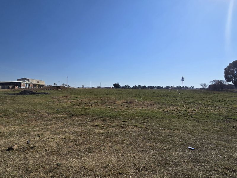 A wide-angle view of a large, flat, vacant commercial plot of land with grass cover, suitable for future development.