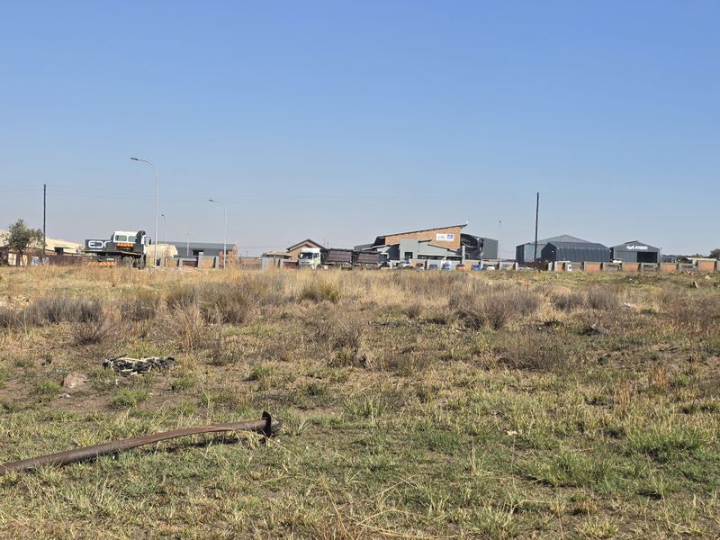 A view of a vacant commercial land plot with surrounding industrial infrastructure and street lighting visible in the background.