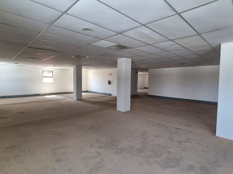 A large, open-plan office space featuring a suspended ceiling, structural columns, and essential fire safety equipment, ready for custom fit-out.