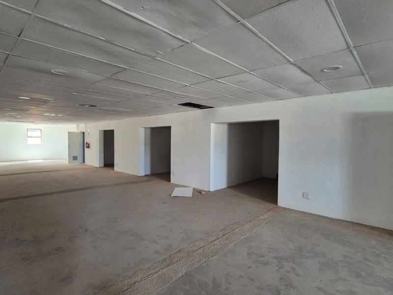 Spacious open-plan office area featuring a suspended ceiling with recessed lighting and multiple partitioned entryways, currently in need of refurbishment.
