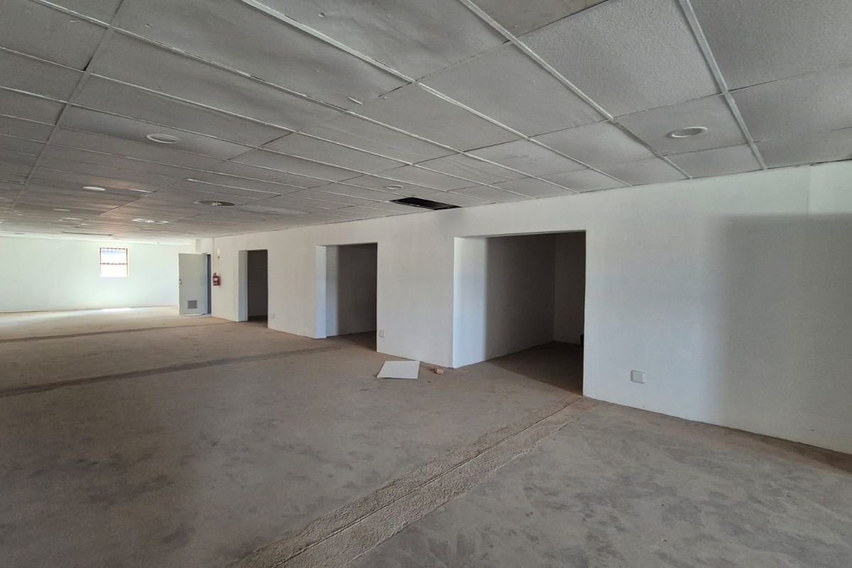 Spacious open-plan office area featuring a suspended ceiling with recessed lighting and multiple partitioned entryways, currently in need of refurbishment.