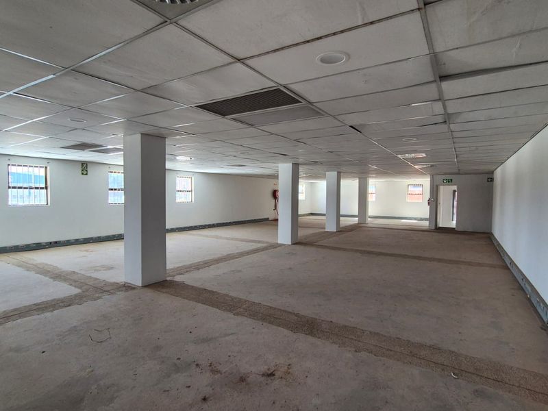A large, open-plan office space featuring structural columns, a suspended ceiling, and security-barred windows, currently in a shell-like condition ready for fit-out.