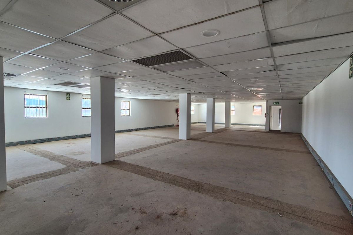 A large, open-plan office space featuring structural columns, a suspended ceiling, and security-barred windows, currently in a shell-like condition ready for fit-out.