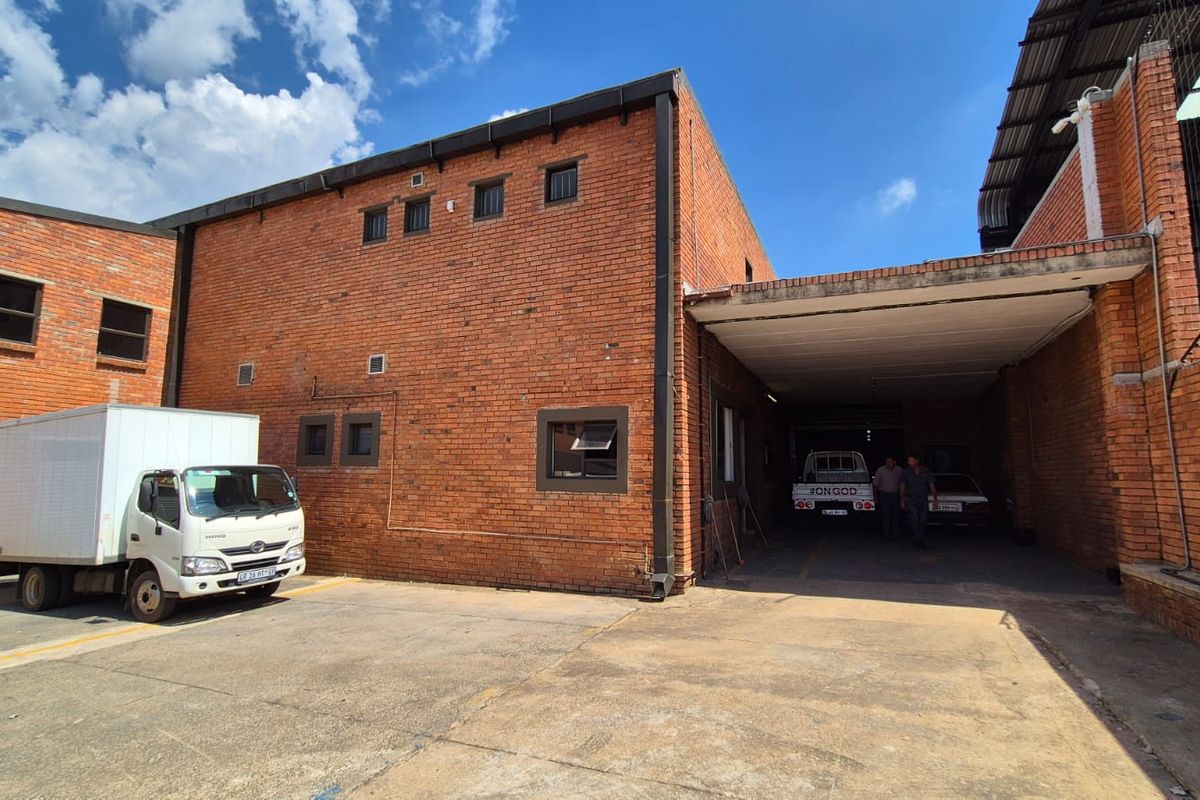 Rear exterior view of an industrial office building featuring exposed brickwork, a covered loading bay area, and a concrete driveway.