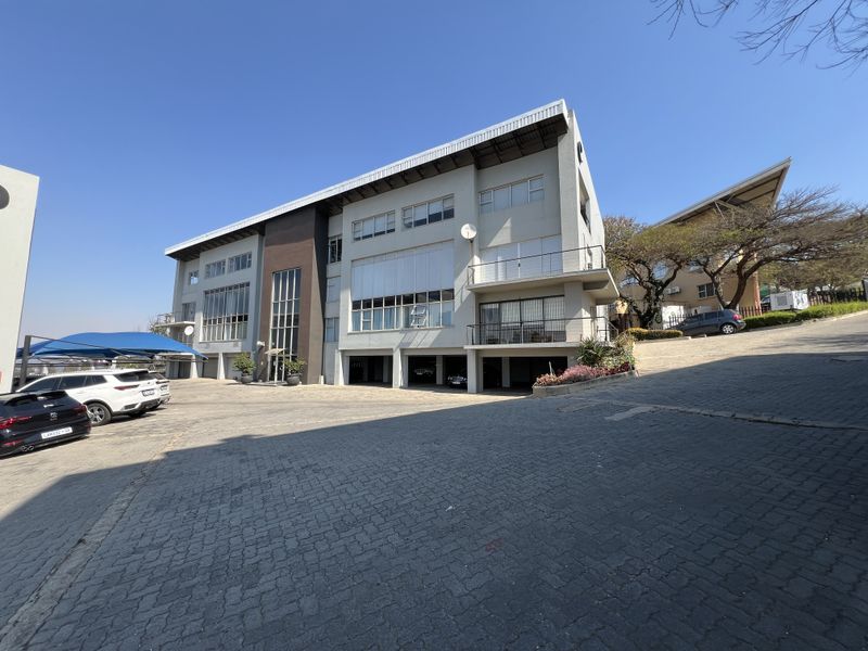 A multi-story office building featuring a paved driveway, covered parking areas, and modern architectural design with large windows and balconies.