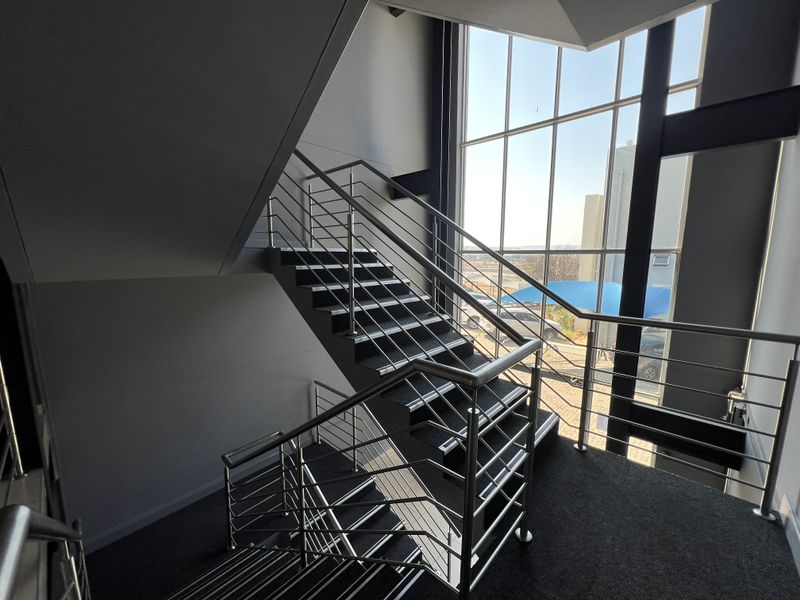 Modern office staircase featuring a stainless steel balustrade and a large, full-height glass curtain wall providing ample natural light.