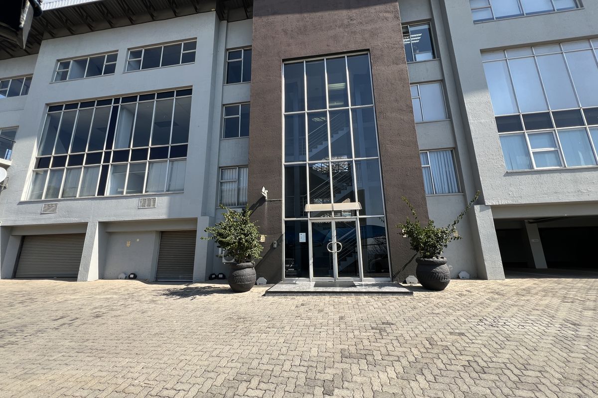 Modern office building facade featuring a prominent glass entrance, large windows, and paved driveway with integrated roller shutter garage access.