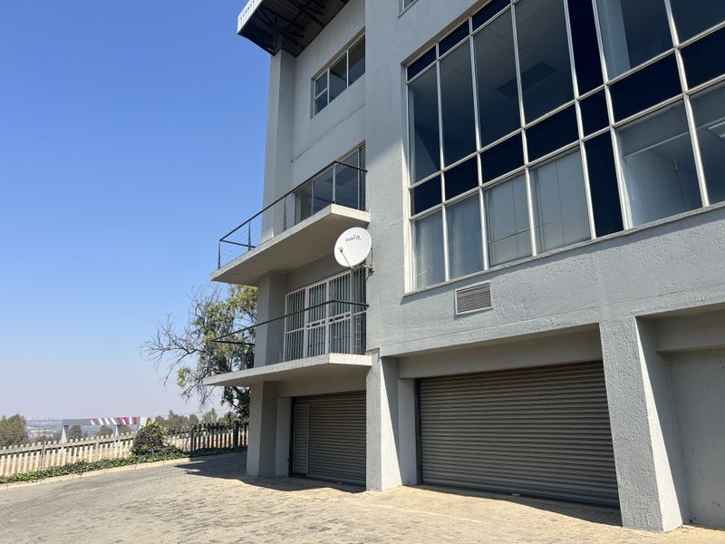 Rear elevation of a multi-story office building featuring roller shutter garage doors, balconies with glass railings, and large glass facade panels.
