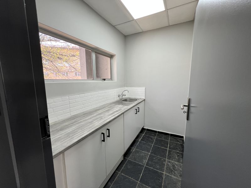 A clean and functional kitchenette or utility area featuring built-in cabinetry, a laminate countertop, stainless steel sink, and modern tiled backsplash.