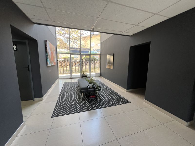 Modern office building entrance lobby featuring tiled flooring, a suspended ceiling, and large glass doors providing ample natural light.