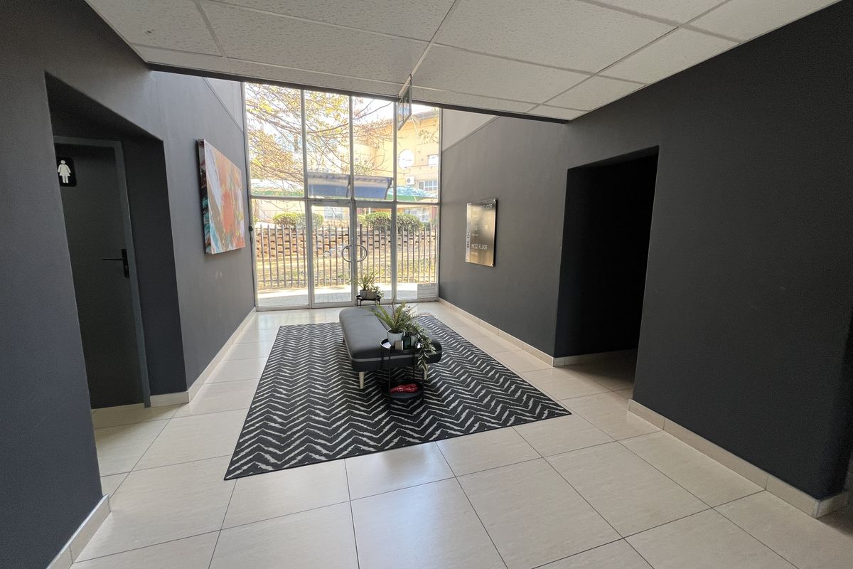 Modern office building entrance lobby featuring tiled flooring, a suspended ceiling, and large glass doors providing ample natural light.