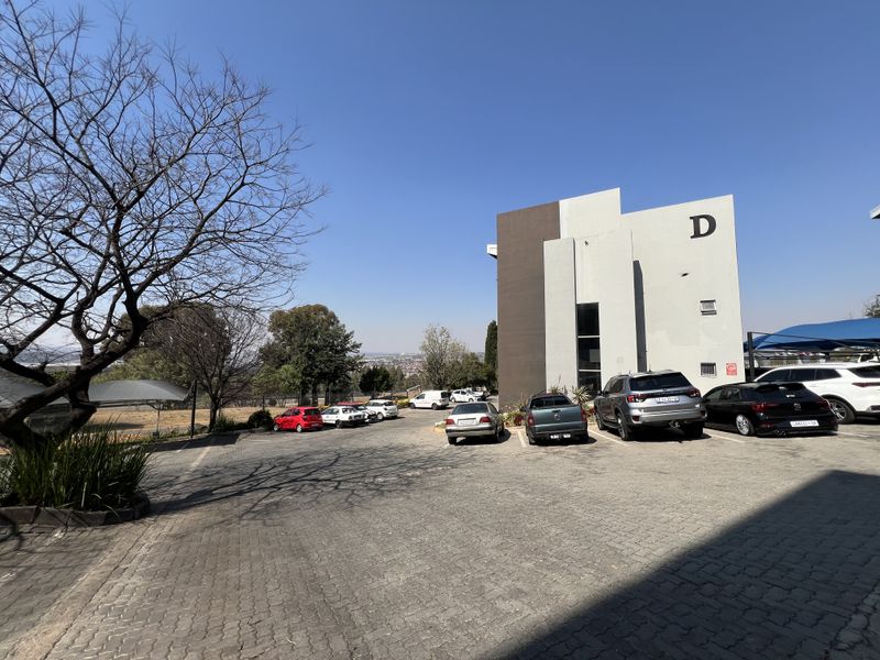 Exterior view of a modern office building block D with extensive paved parking and shade cloth carports.