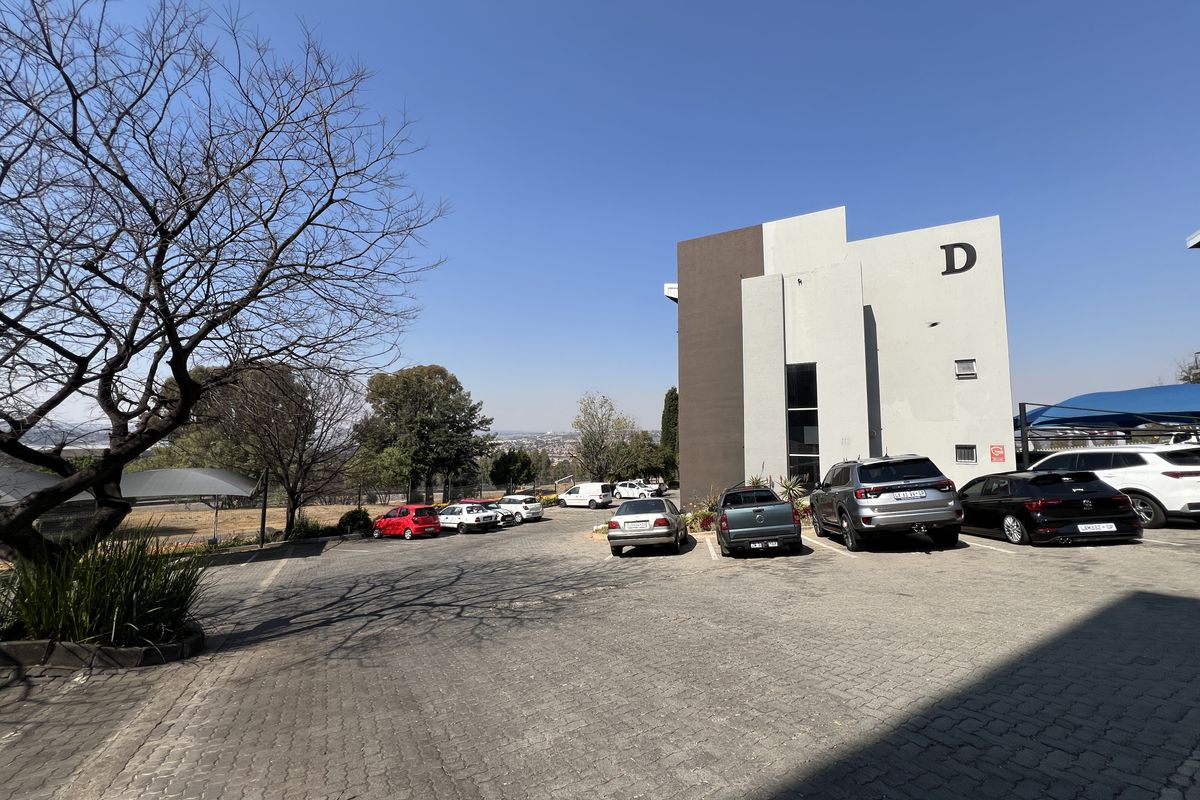 Exterior view of a modern office building block D with extensive paved parking and shade cloth carports.