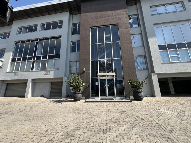 Modern office building facade featuring a prominent glass entrance, large windows, and paved driveway with integrated roller shutter garage access.