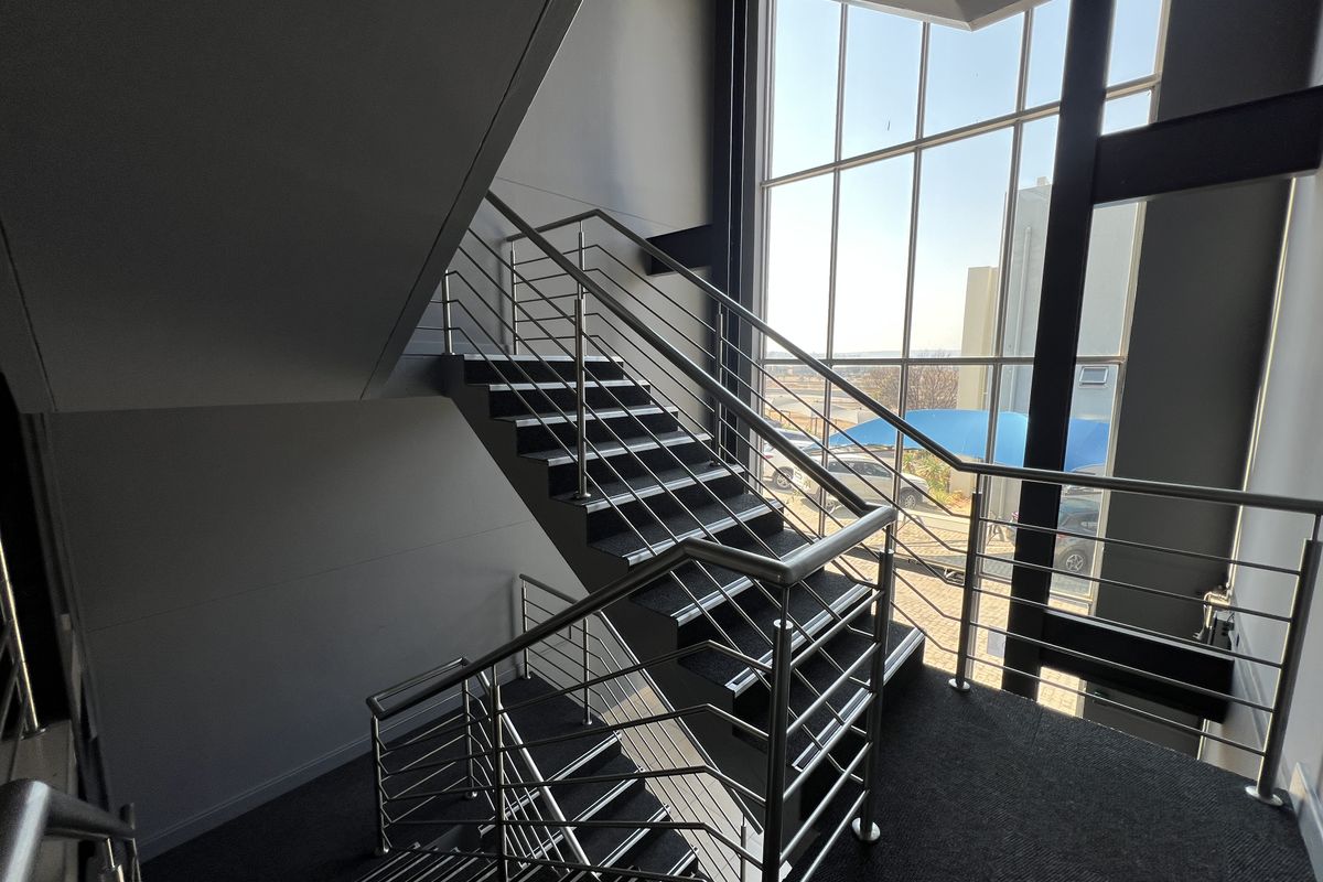 Modern office staircase featuring a stainless steel balustrade and a large, full-height glass curtain wall providing ample natural light.
