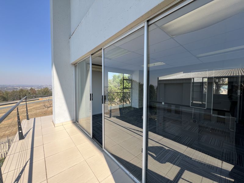 A spacious balcony with tiled flooring and metal railings, providing access to an interior office space through large sliding glass doors.