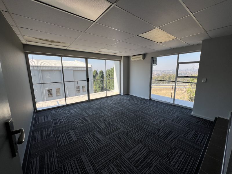A vacant office space featuring carpet tiles, a suspended ceiling, and large sliding glass doors providing natural light and scenic views.