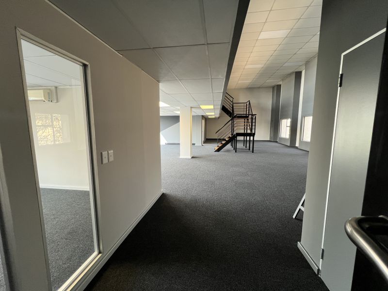 Spacious open-plan office area featuring a modern metal staircase, suspended ceilings, and neutral carpeting, offering a clean and professional workspace environment.