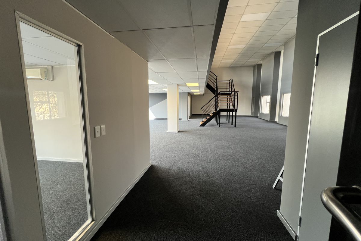 Spacious open-plan office area featuring a modern metal staircase, suspended ceilings, and neutral carpeting, offering a clean and professional workspace environment.