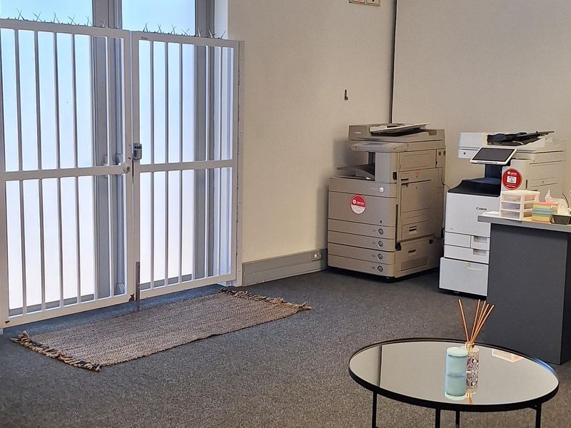 A functional commercial office space featuring carpeted flooring, a suspended ceiling with recessed lighting, and a secure aluminium-framed glass entrance door.