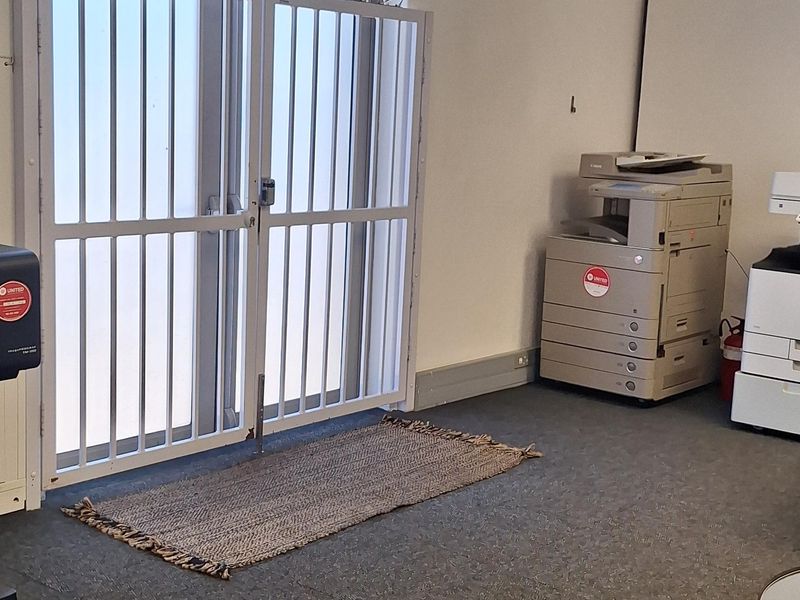 A functional office space featuring carpeted flooring, a suspended ceiling, and a secure metal entrance gate.