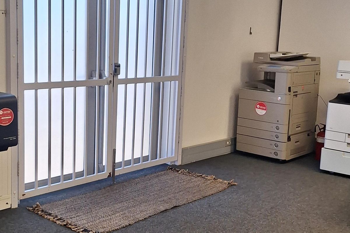 A functional office space featuring carpeted flooring, a suspended ceiling, and a secure metal entrance gate.