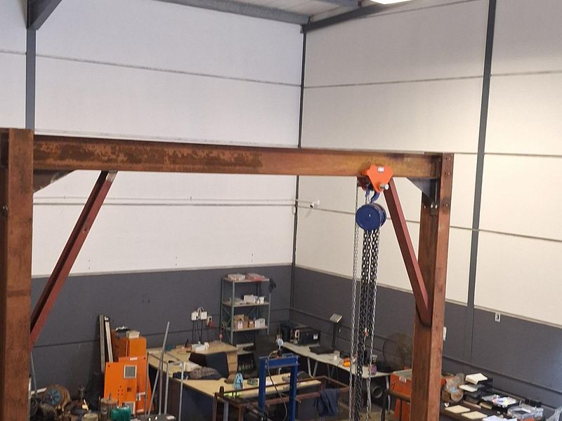 A high-volume industrial utility space featuring exposed steel roof trusses, concrete flooring, and an integrated gantry crane for heavy equipment handling.