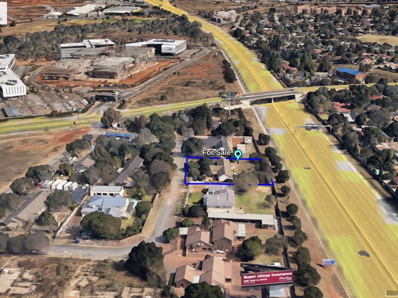 Aerial view of a vacant commercial property plot highlighted in blue, situated in a developed suburban area with mature trees.