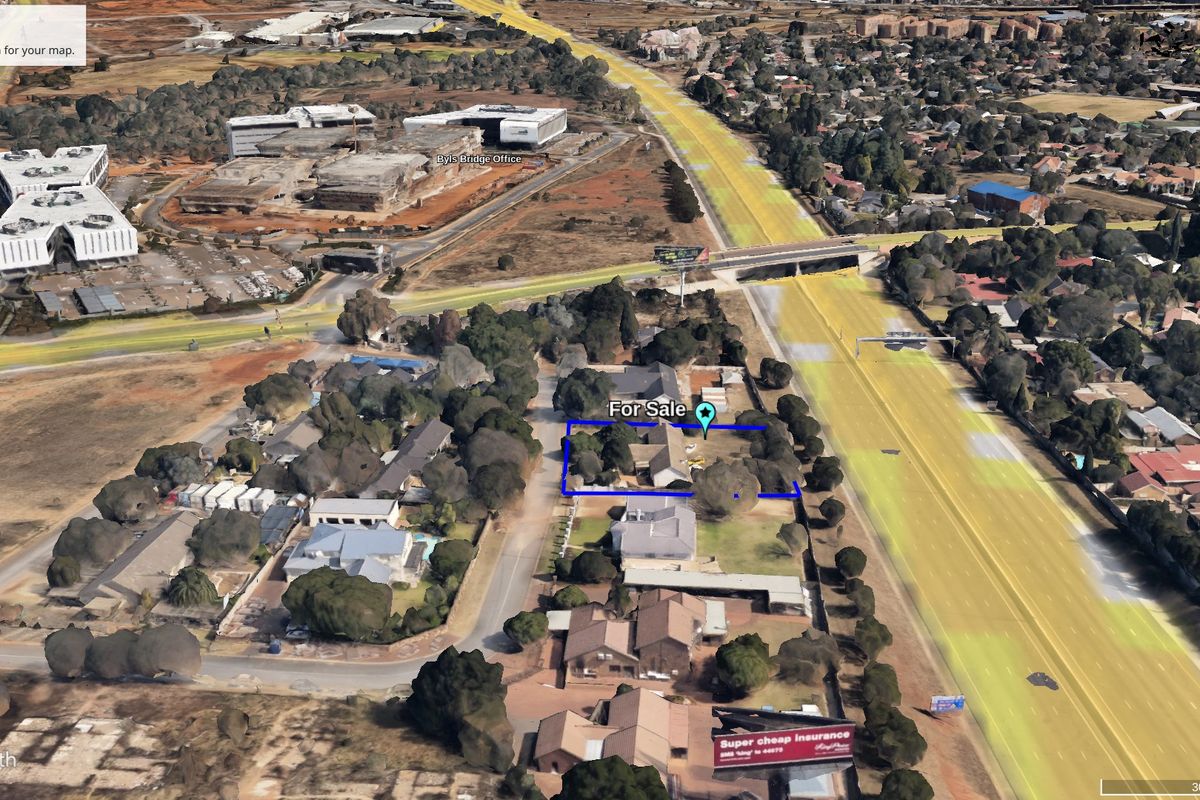 Aerial view of a vacant commercial property plot highlighted in blue, situated in a developed suburban area with mature trees.