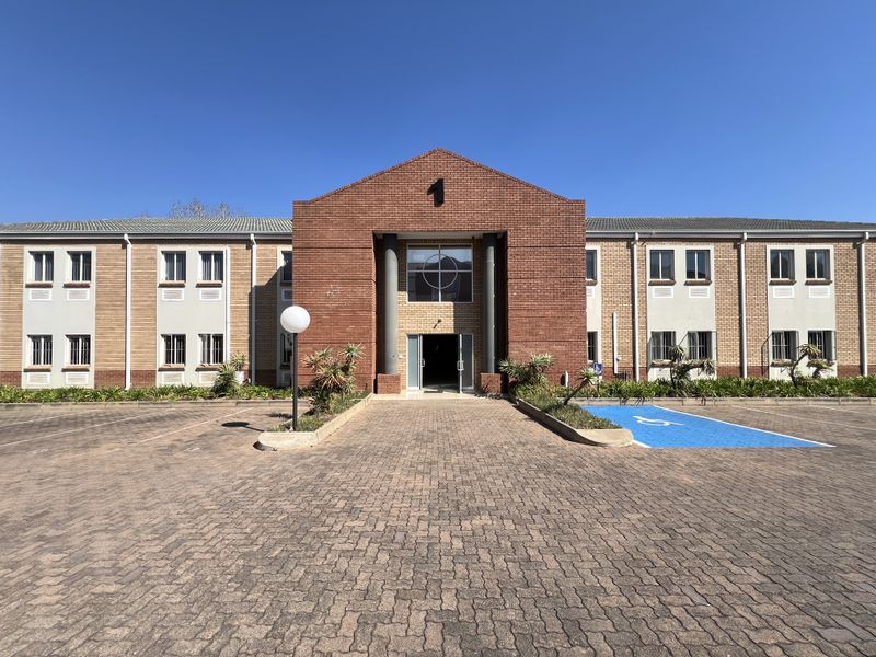 Front elevation of a two-story brick office building featuring a prominent central entrance, paved parking area, and designated accessible parking bay.