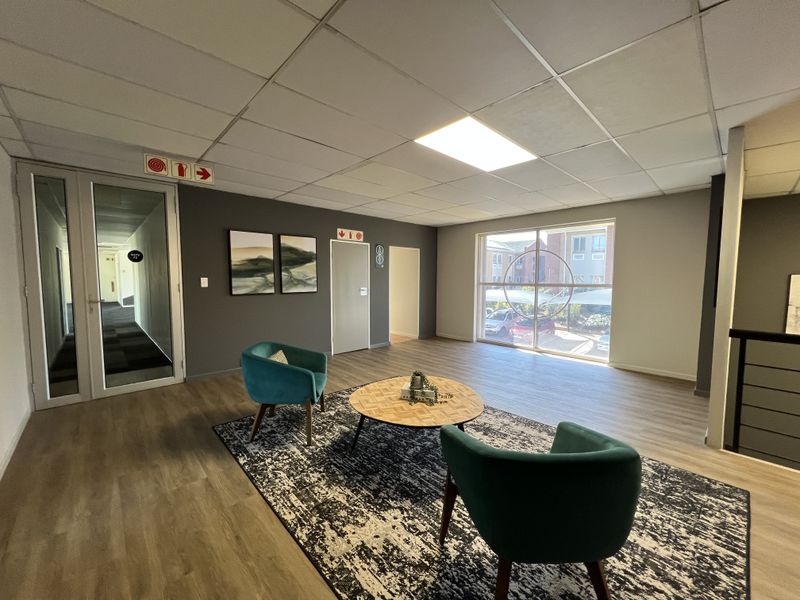 A bright and modern office reception or waiting area featuring laminate flooring, a suspended ceiling, and large windows providing natural light.