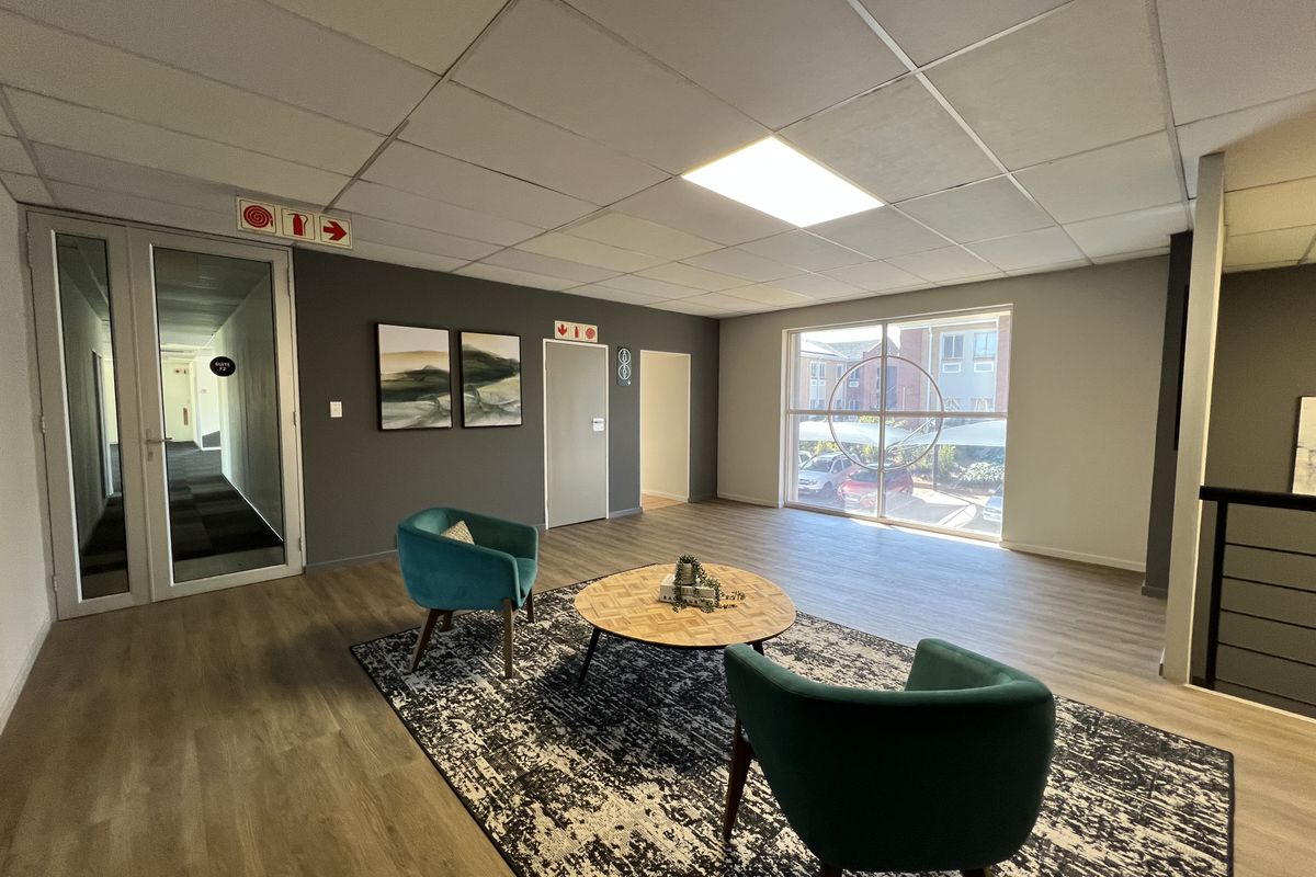 A bright and modern office reception or waiting area featuring laminate flooring, a suspended ceiling, and large windows providing natural light.