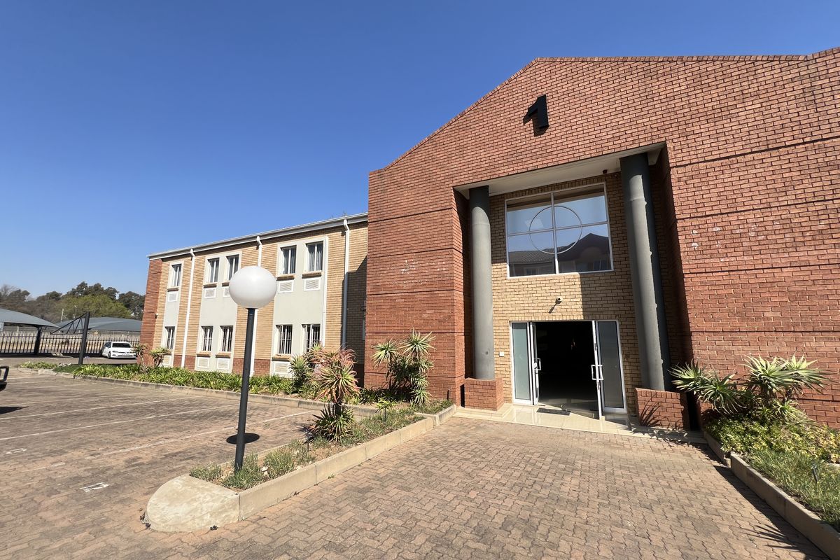 Front exterior view of a professional office building featuring a red brick facade, paved parking area, and a prominent entrance with structural columns.