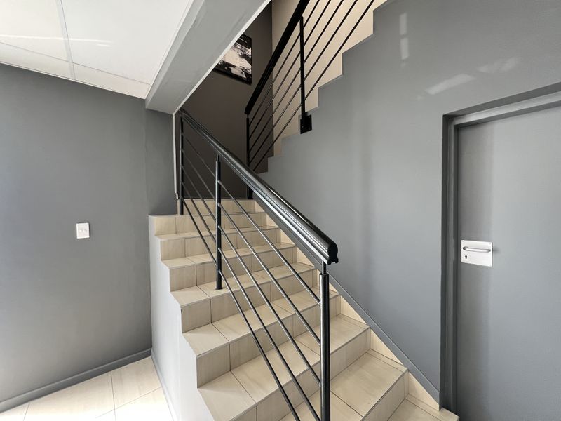 A clean, modern office hallway featuring a tiled staircase with a sleek black metal balustrade and handrail.