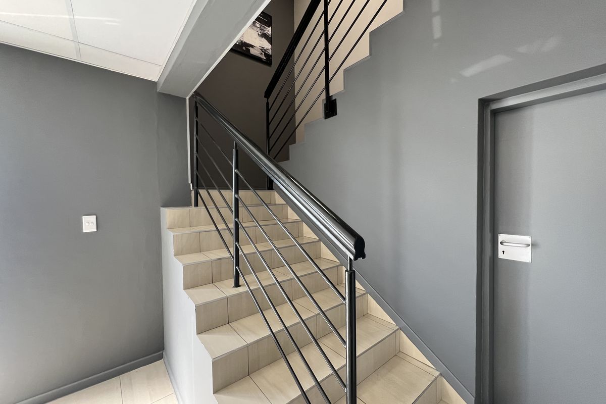 A clean, modern office hallway featuring a tiled staircase with a sleek black metal balustrade and handrail.