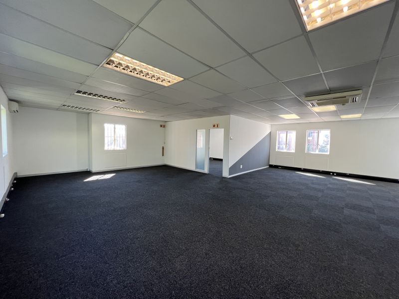 A spacious, open-plan office area featuring carpeted flooring, suspended ceilings with recessed lighting, and integrated air conditioning.