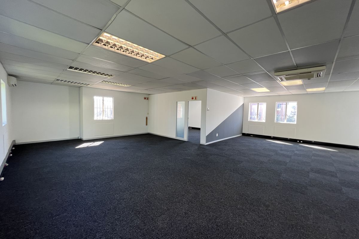 A spacious, open-plan office area featuring carpeted flooring, suspended ceilings with recessed lighting, and integrated air conditioning.