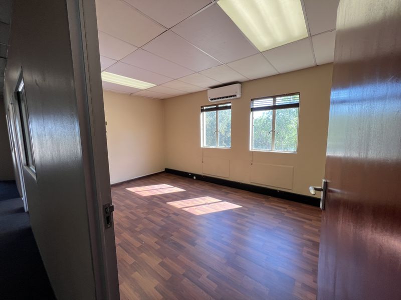 A vacant office space featuring laminate flooring, a suspended ceiling with recessed lighting, and a wall-mounted split-system air conditioning unit.