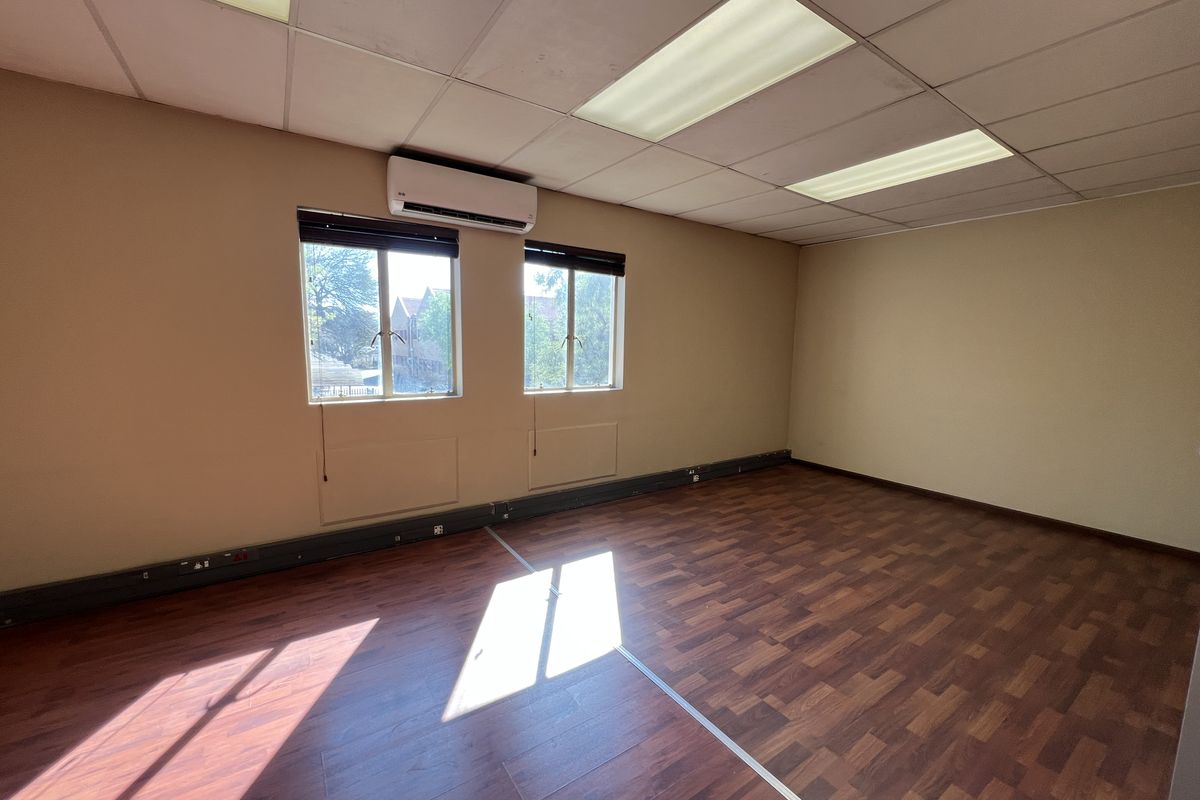 A vacant office space featuring laminate wood flooring, suspended ceiling with recessed lighting, and a wall-mounted split-system air conditioning unit.