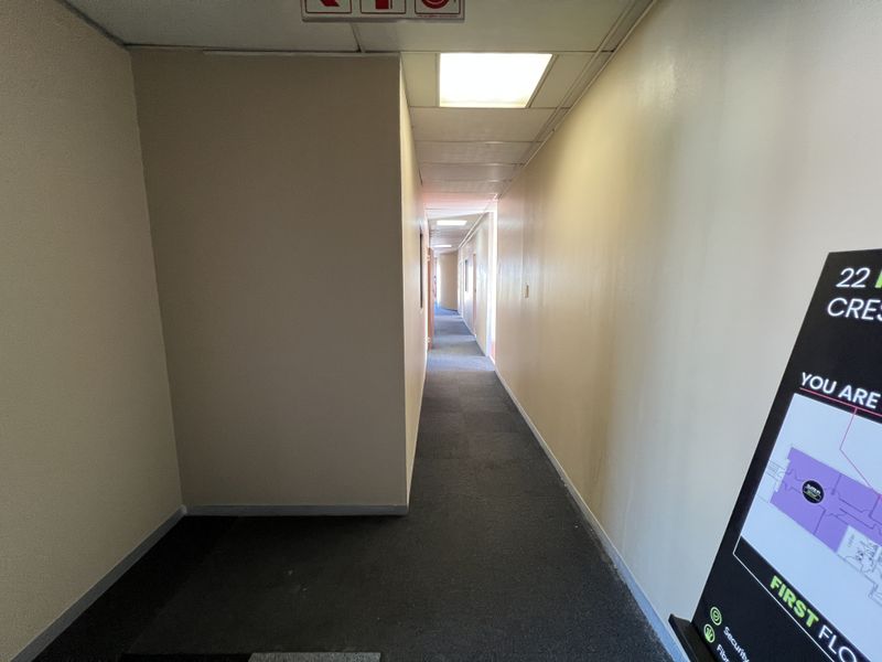 A long, functional office building hallway featuring recessed ceiling lighting and carpeted flooring, providing access to various office suites.