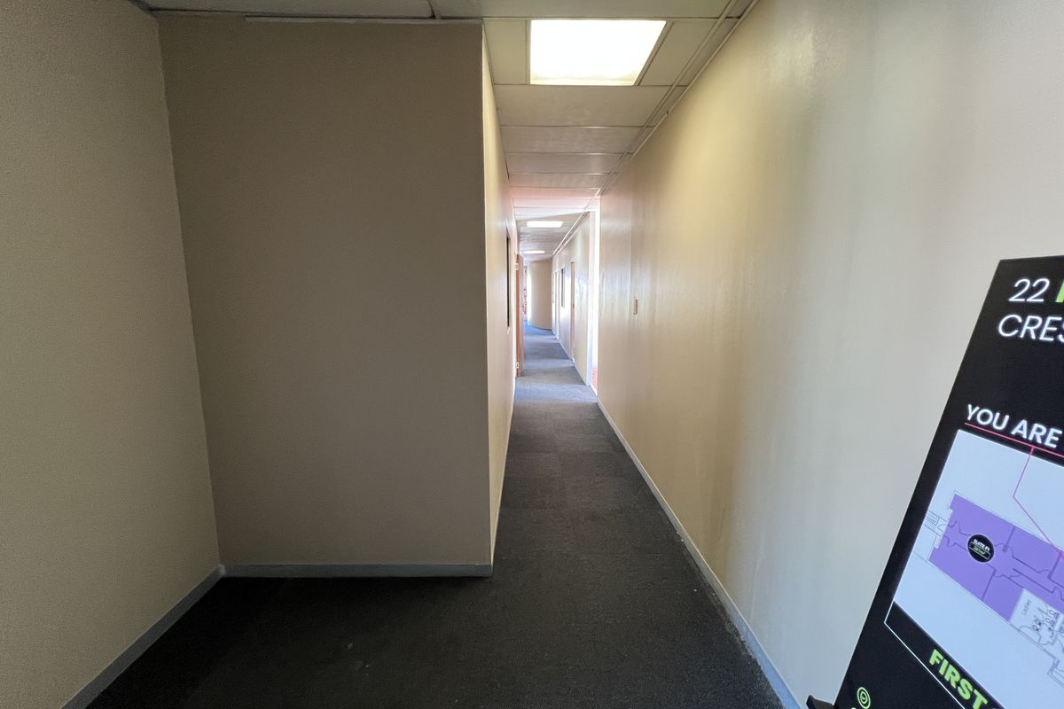 A long, functional office building hallway featuring recessed ceiling lighting and carpeted flooring, providing access to various office suites.