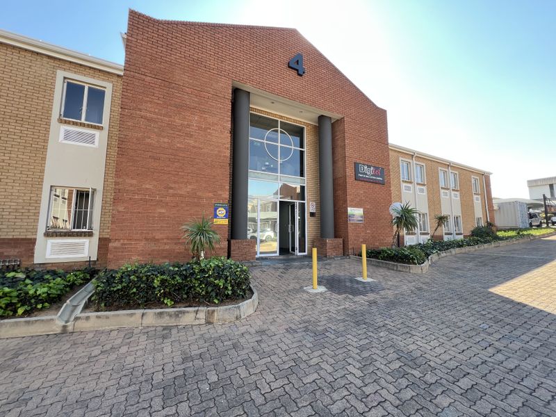 Front elevation of a commercial office building featuring a prominent brick facade, glass entrance, and paved driveway access.
