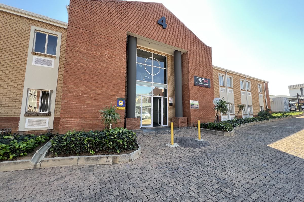Front elevation of a commercial office building featuring a prominent brick facade, glass entrance, and paved driveway access.