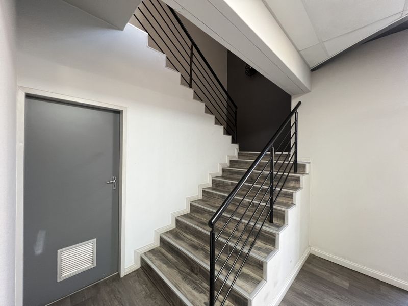 A clean, modern office hallway featuring a staircase with metal balustrades and durable laminate flooring.