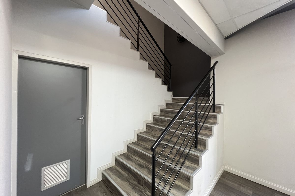 A clean, modern office hallway featuring a staircase with metal balustrades and durable laminate flooring.