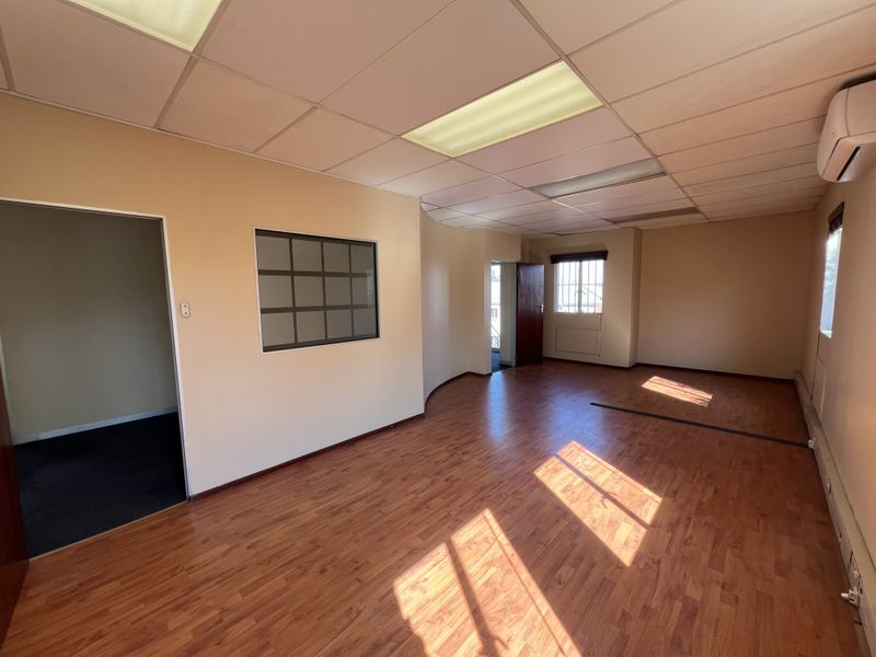 An empty office space featuring laminate flooring, a suspended ceiling with recessed lighting, and a wall-mounted air conditioning unit.
