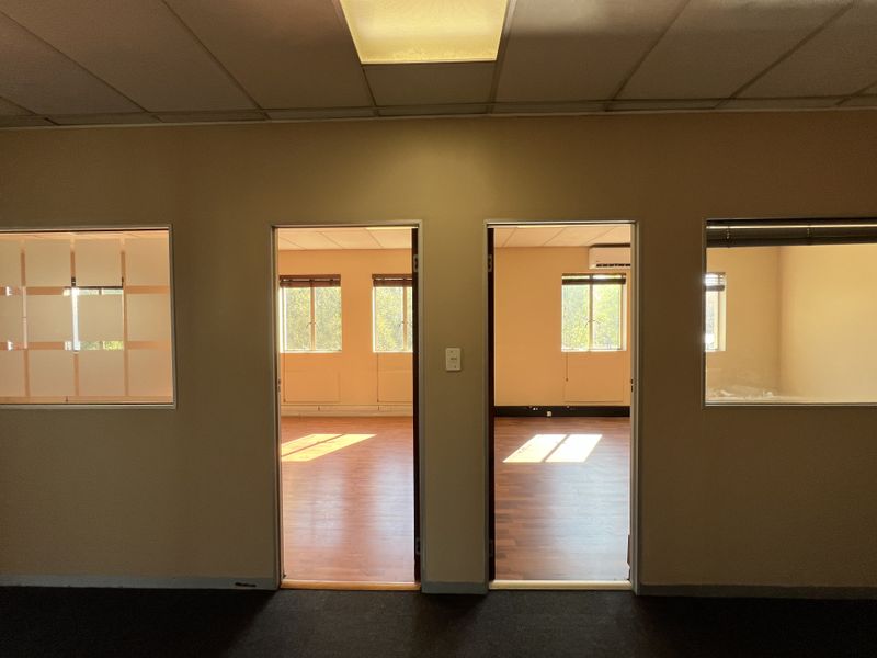 Empty office space featuring laminate flooring, suspended ceilings, and internal glass partitions providing views into adjacent work areas.