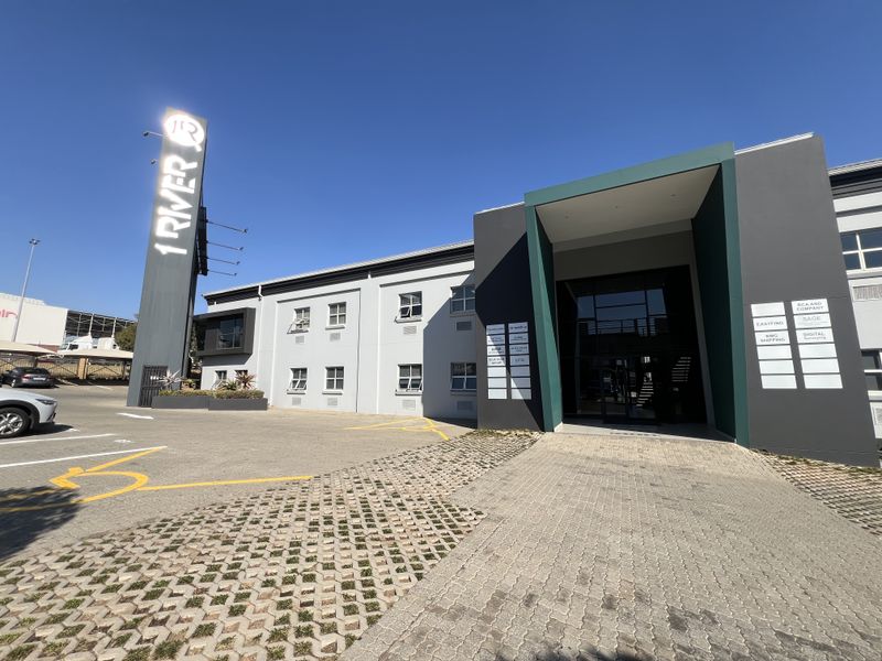 Modern commercial office building exterior featuring a prominent pylon sign, paved parking area, and a contemporary glass-fronted entrance with tenant directory signage.